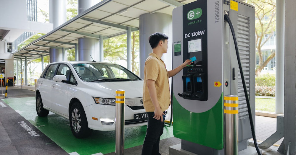 A driver operating an EV charger beside a passenger vehicle.