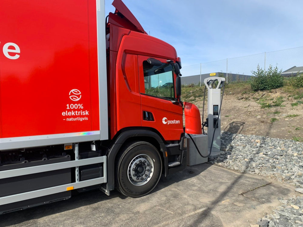 A commercial truck connected to charging equipment at an outdoor site.
